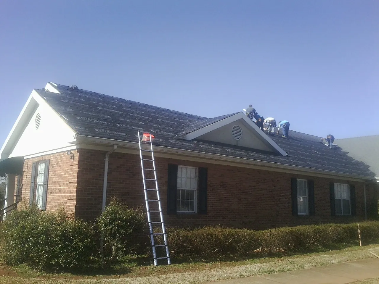 Crew tearing shingles off a brick ranch roof with a ladder set — Metal Roof Repair work by our crew in Blountsville