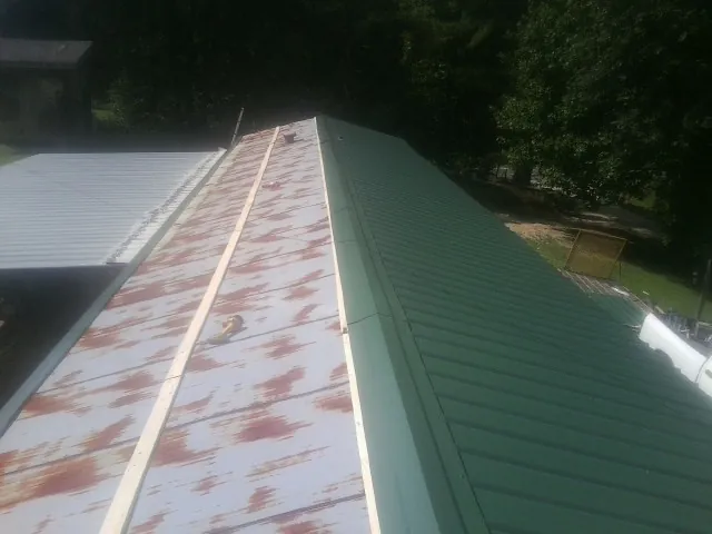 Old rusted panels beside newly installed green metal roofing — Wind Damage Roof Repair by Roofing Brothers in Blountsville