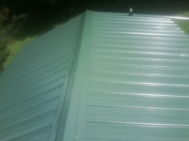 New green metal panels meeting at the ridge of a roof — Flat Roof Repair work by our crew in Blountsville
