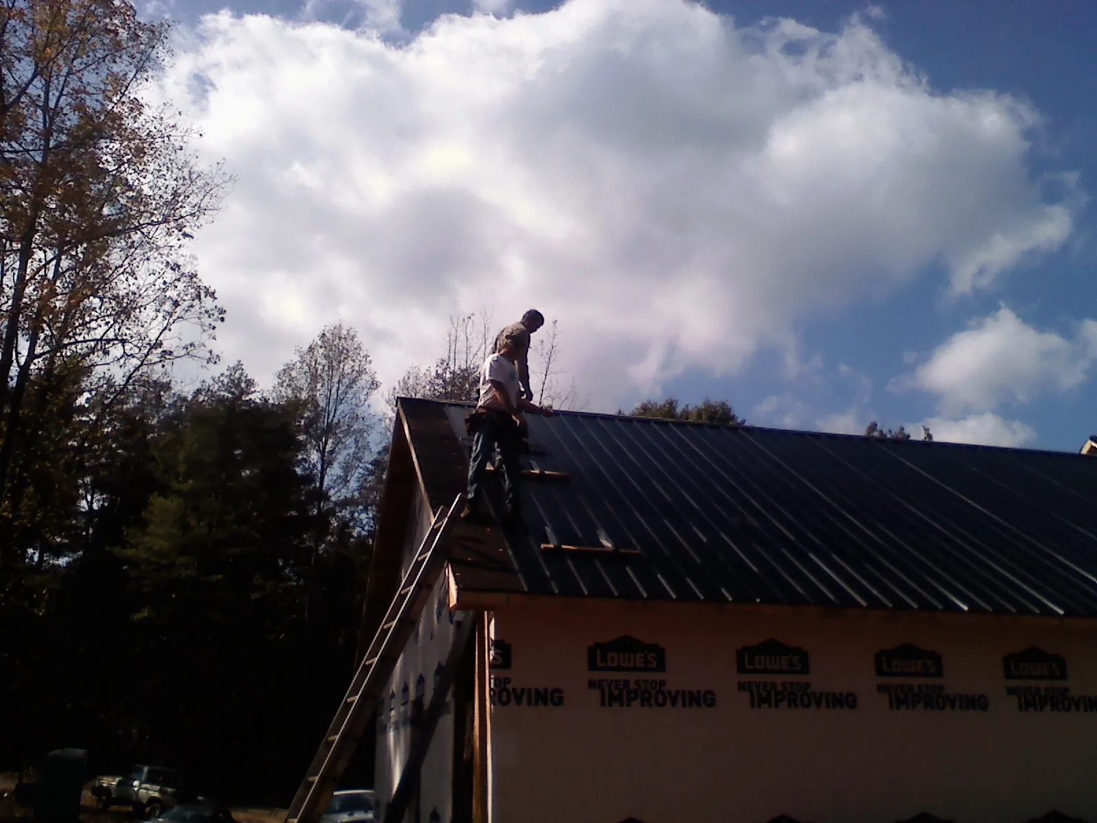 Roofer fastening dark metal panels high against a cloudy sky, from a Roof Inspection job in Blountsville