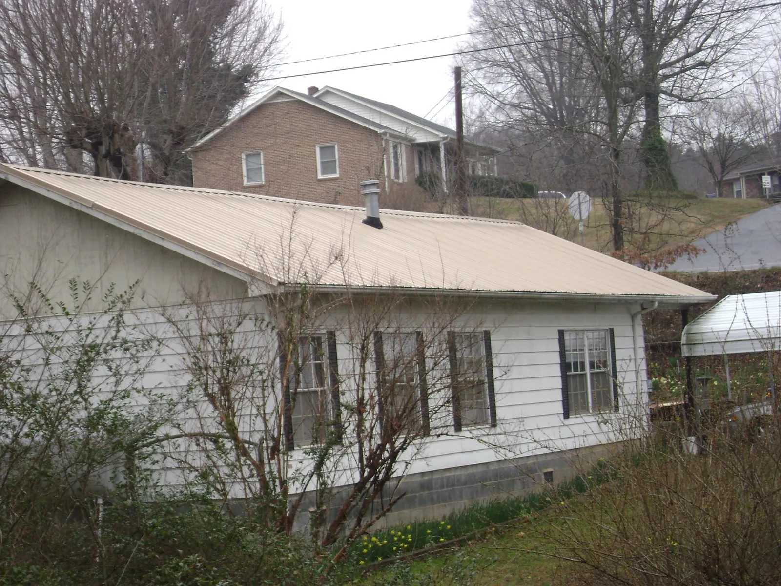 Tan metal roof on a white sided house set into a hillside — Commercial Roofing by Roofing Brothers in Blountsville
