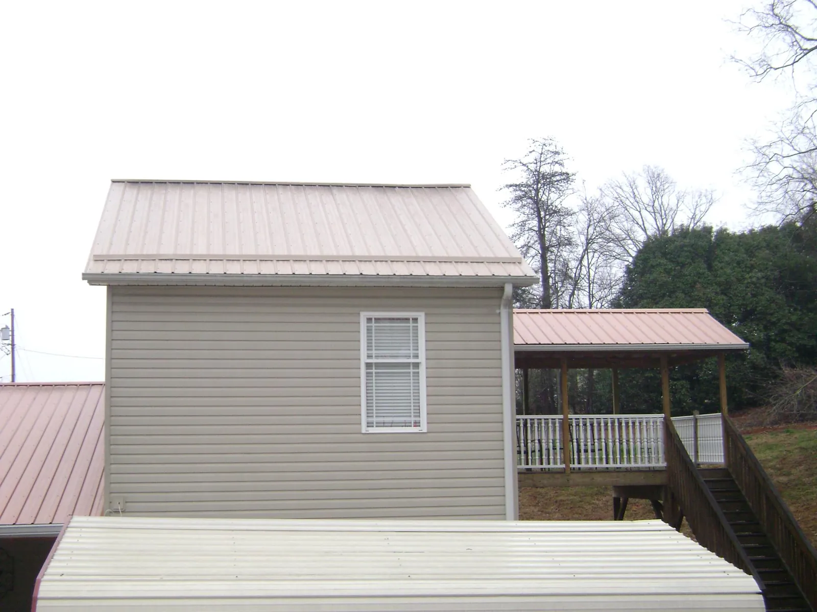 Tan metal roofs on a two story addition and attached porch, from a Roof Replacement job in Blountsville